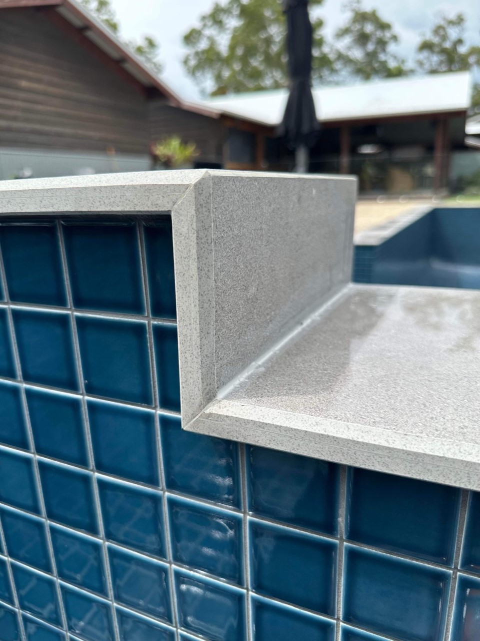 edge of a pool with shiny blue tile capped with light grey tiles