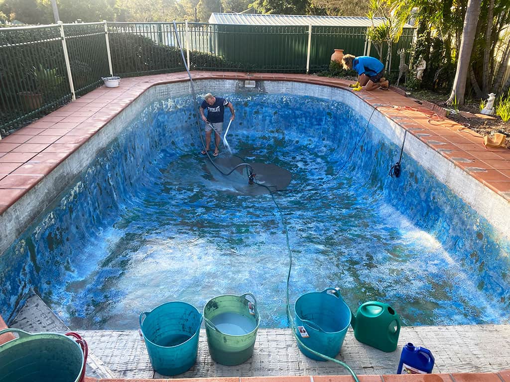 Man in empty pool cleaning it with a hose
